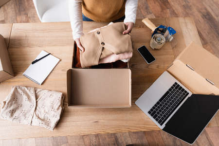 partial view of showroom owner holding clothes near carton boxes and gadgets at workplaceの写真素材