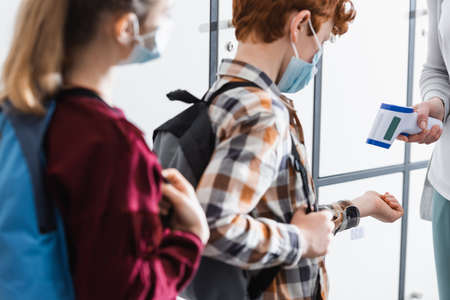 Teacher checking temperature of pupil with infrared thermometer during quarantine