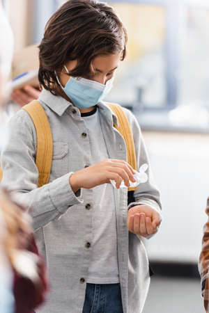 Schoolboy in protective mask using hand sanitizer in schoolの写真素材