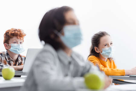 pupils in medical masks listening during lesson on blurred foreground