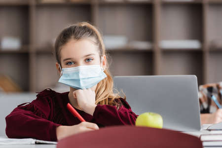 schoolgirl in medical mask looking at camera on blurred foregroundの写真素材