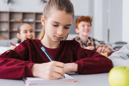 schoolgirl writing in notebook during lesson on blurred foregroundの写真素材