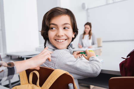schoolkid touching cheerful classmate during lesson in classroom, blurred backgroundの写真素材