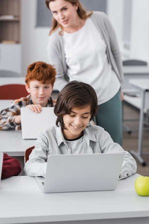 teacher standing near pupils using laptops during lesson, blurred background