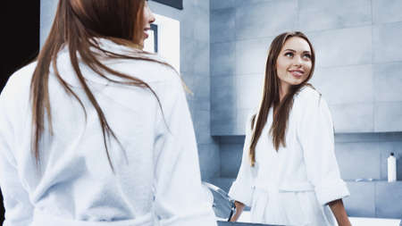 cheerful young woman in bathrobe smiling in bathroomの写真素材