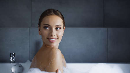 cheerful young woman looking away while taking bath at home