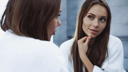 young and pretty woman in bathrobe looking at mirrorの写真素材