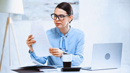 serious businesswoman working with documents near laptop in office