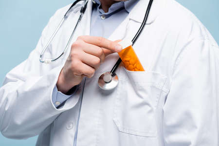 cropped view of doctor in white coat with stethoscope putting bottle with medication in pocket...