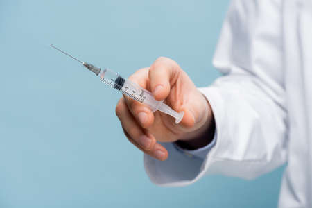 cropped view of doctor holding syringe in hand isolated on blueの写真素材