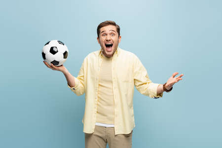 amazed man in yellow shirt holding football on blueの写真素材