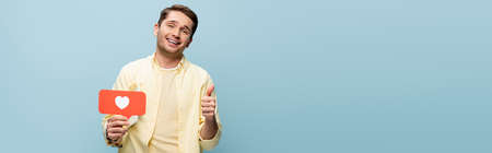 happy man in shirt holding red paper heart and showing thumb up isolated on blue, banner