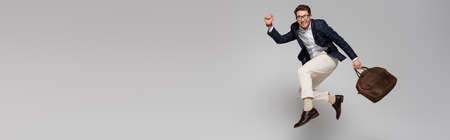 full length of cheerful businessman with leather bag levitating on gray, bannerの写真素材
