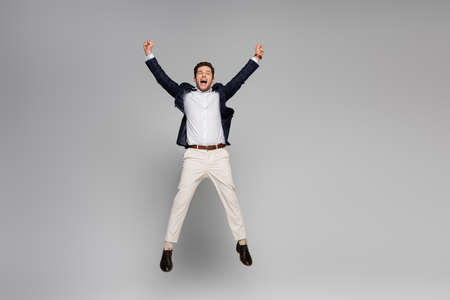 full length of excited man with outstretched hands jumping on grayの写真素材