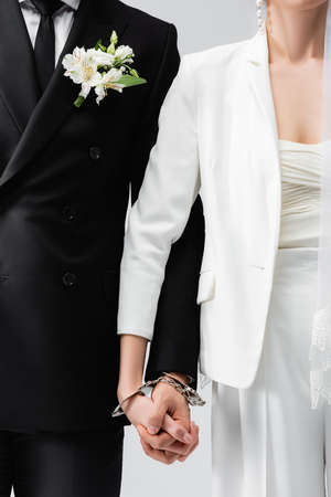 Cropped view of bride and groom holding hands in handcuffs isolated on grayの写真素材