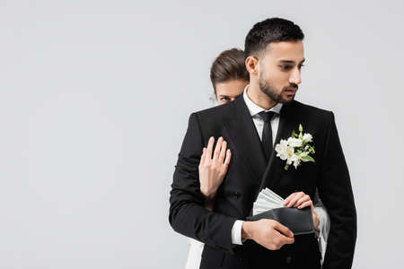 Bride taking dollars from wallet in hand of arabian groom isolated on gray