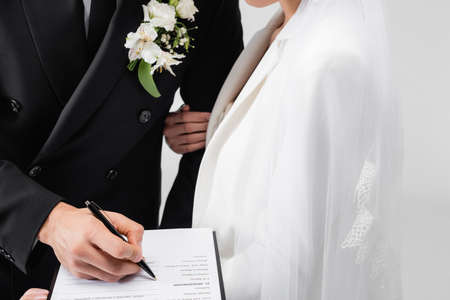 Cropped view of groom signing wedding contract near young bride isolated on grayの写真素材