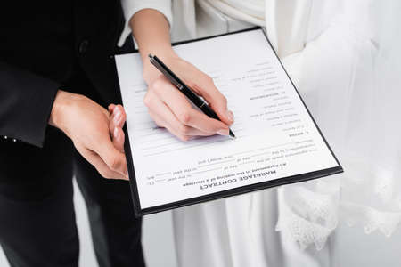 Cropped view of couple signing marriage contract isolated on gray