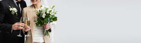 Cropped view of smiling bride toasting champagne with groom isolated on gray, banner