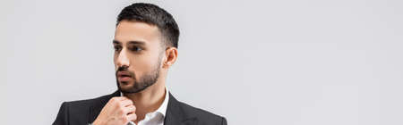 elegant arabian man touching chin while looking away isolated on gray, bannerの写真素材