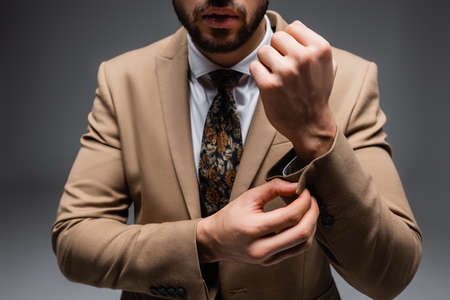cropped view of stylish muslim man buttoning sleeve on blazer on grayの写真素材
