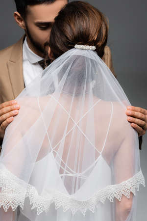 arabian man hugging shoulders of bride in veil isolated on grayの写真素材