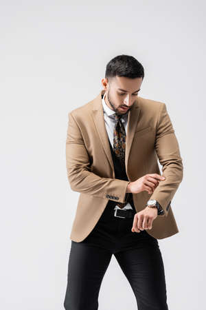 fashionable arabian man checking time on wristwatch while posing isolated on grayの写真素材