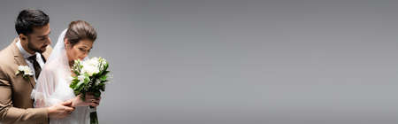 arabian  groom hugging bride smelling bouquet isolated on gray, bannerの写真素材