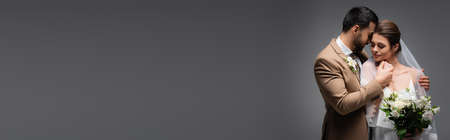 elegant, interracial newlywed couple holding hands while standing on gray, bannerの写真素材