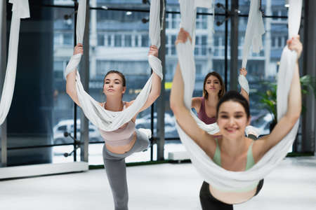 group of young sportswomen stretching with straps while practicing aerial yoga, blurred foreground