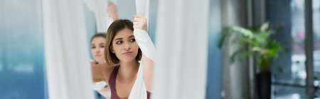 young sportswoman looking away while training with fly yoga hammock, blurred foreground, bannerの写真素材