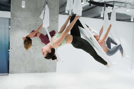 young sportive women practicing aerial yoga in sports center, blurred backgroundの写真素材