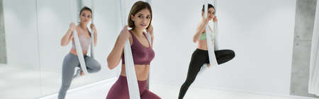 young sportswomen stretching legs with aerial yoga straps, bannerの写真素材