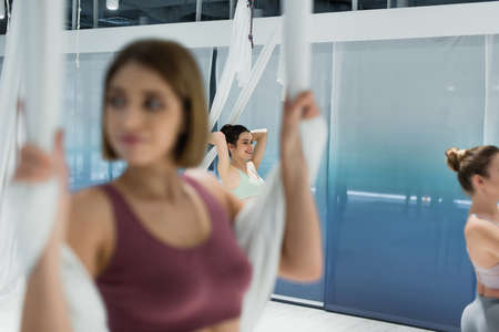 selective focus of smiling woman warming up with aerial yoga hammock on blurred foregroundの写真素材