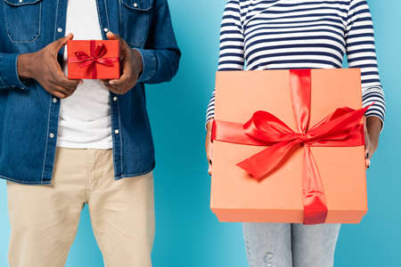 cropped view of african american couple holding big and small gift boxes on blueの写真素材