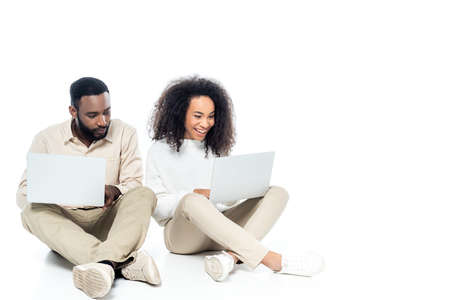 curious african american man looking at laptop in hands of cheerful wife on whiteの写真素材