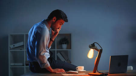 businessman looking at laptop while working late in officeの写真素材