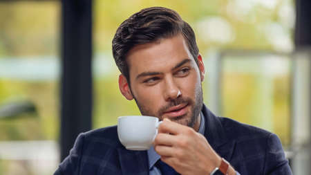 handsome businessman holding cup of coffee and looking awayの写真素材