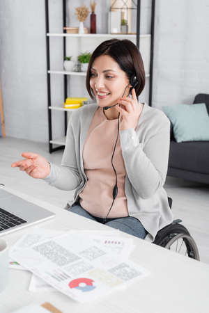 Handicapped freelancer using headset and laptop near papers on blurred foreground