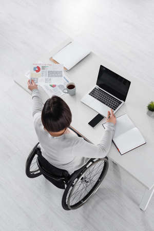 Overhead view of handicapped woman working with devices, papers and coffee