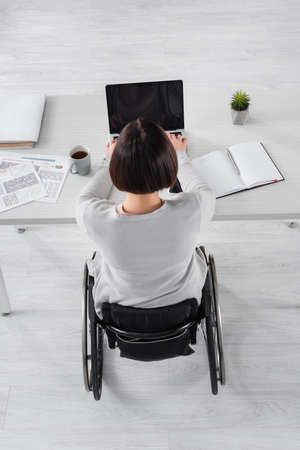 Overhead view of handicapped woman using laptop near cup of coffee and papers on tableの写真素材