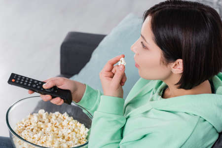 Brunette woman with remote controller holding popcorn
