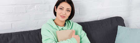 Smiling woman holding book on couch, banner