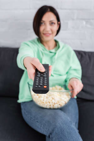 Remote controller in hand of smiling woman with popcorn on blurred backgroundの写真素材