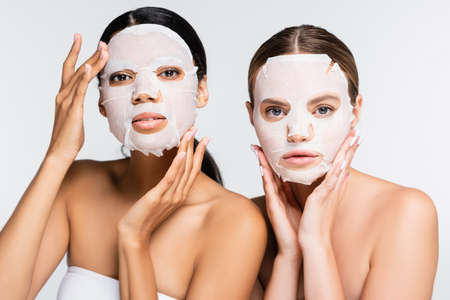 young multiethnic women in moisturizing sheet masks isolated on whiteの写真素材