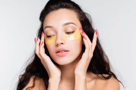 brunette young woman with bare shoulders touching eye patches isolated on whiteの写真素材