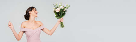 excited fiancee showing win gesture while holding wedding bouquet isolated on gray, bannerの写真素材