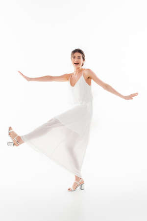 full length view of cheerful bride looking at camera while dancing on whiteの写真素材