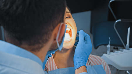 dentist in medical mask examining teeth of woman in clinic, blurred foregroundの写真素材