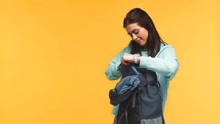 young traveler packing backpack isolated on yellowの写真素材
